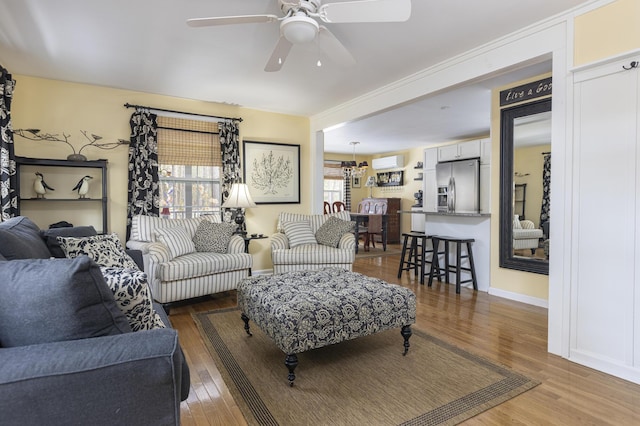 living room featuring a wall mounted air conditioner, baseboards, a ceiling fan, and wood finished floors