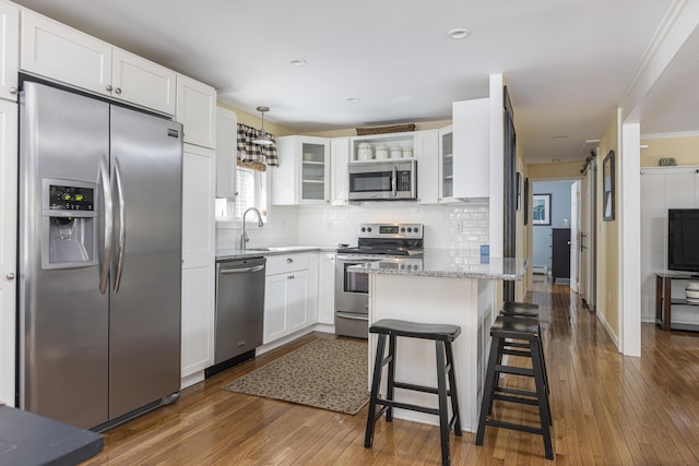 kitchen with glass insert cabinets, light stone counters, decorative backsplash, appliances with stainless steel finishes, and a peninsula