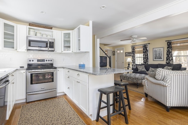 kitchen with light stone countertops, a peninsula, stainless steel appliances, a kitchen bar, and open floor plan