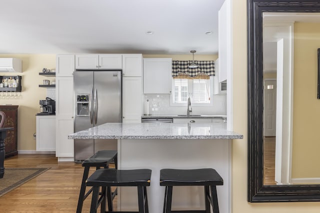 kitchen featuring a wall mounted air conditioner, a sink, a kitchen breakfast bar, white cabinetry, and appliances with stainless steel finishes