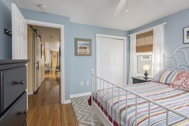 bedroom with a ceiling fan, wood finished floors, baseboards, a closet, and a barn door