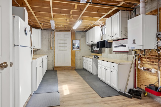 kitchen with light wood finished floors, light countertops, tankless water heater, freestanding refrigerator, and white cabinets