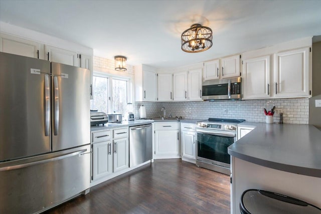 kitchen with a sink, backsplash, dark wood finished floors, stainless steel appliances, and white cabinets