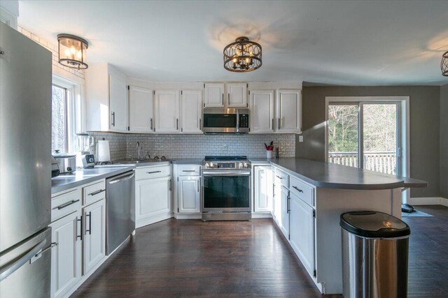 kitchen with a healthy amount of sunlight, a peninsula, stainless steel appliances, white cabinetry, and tasteful backsplash