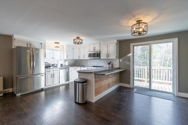 kitchen with dark wood-style floors, a peninsula, appliances with stainless steel finishes, a notable chandelier, and backsplash