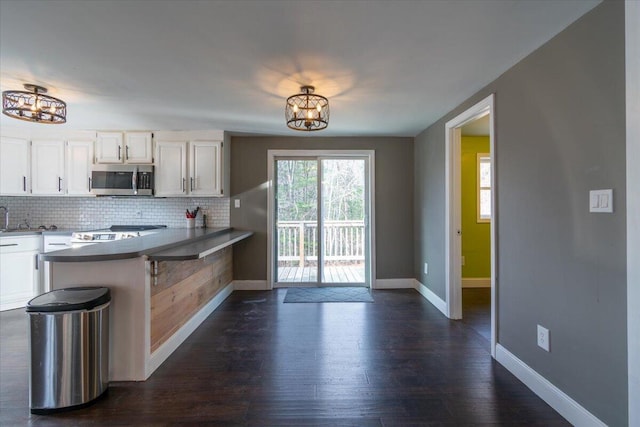 kitchen featuring an inviting chandelier, a peninsula, stainless steel appliances, white cabinetry, and tasteful backsplash