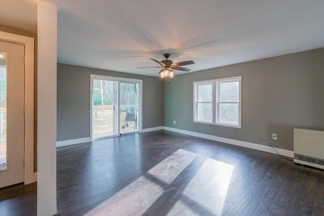 empty room with dark wood finished floors, heating unit, ceiling fan, and baseboards