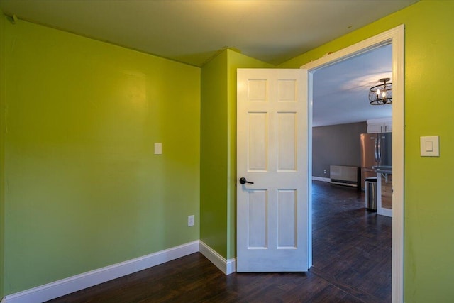 empty room with a chandelier, dark wood-type flooring, and baseboards