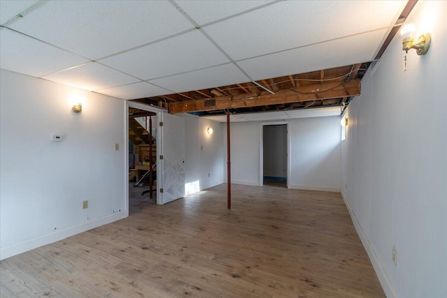 finished basement with a paneled ceiling, baseboards, and wood finished floors