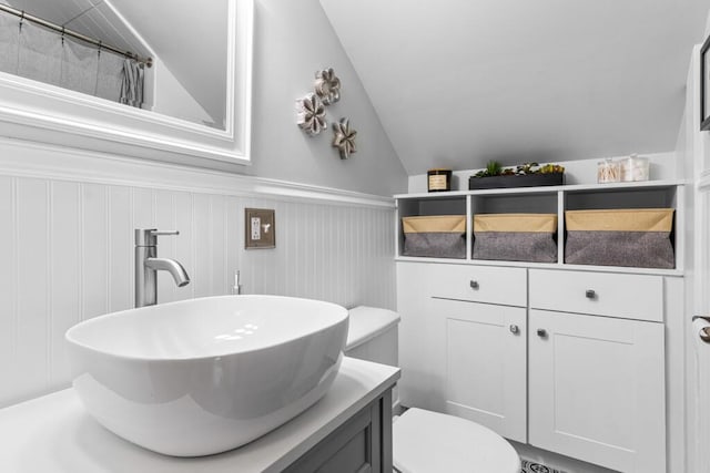 full bathroom featuring vanity, a wainscoted wall, lofted ceiling, curtained shower, and toilet