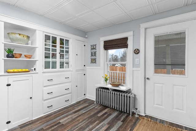 doorway to outside with dark wood finished floors, radiator heating unit, a wainscoted wall, and an ornate ceiling