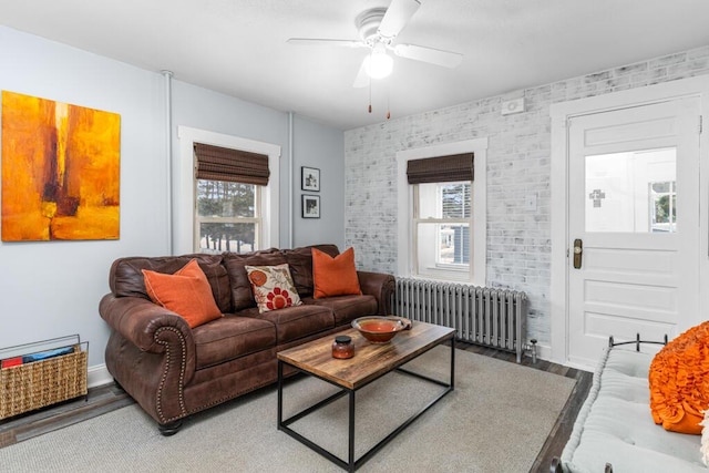 living room featuring a ceiling fan, wood finished floors, radiator, brick wall, and baseboards