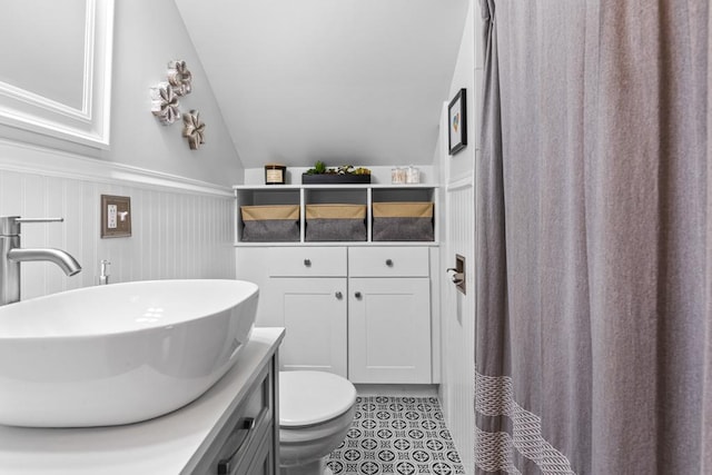 full bathroom featuring vanity, lofted ceiling, wainscoting, tile patterned floors, and toilet