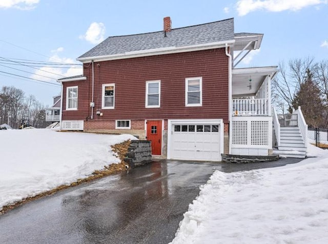 view of snow covered exterior with a shingled roof, stairway, a chimney, a garage, and driveway