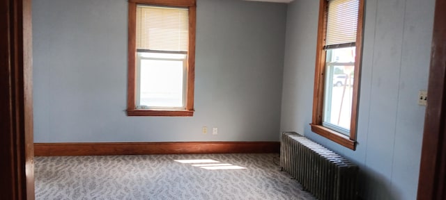 carpeted empty room featuring baseboards and radiator