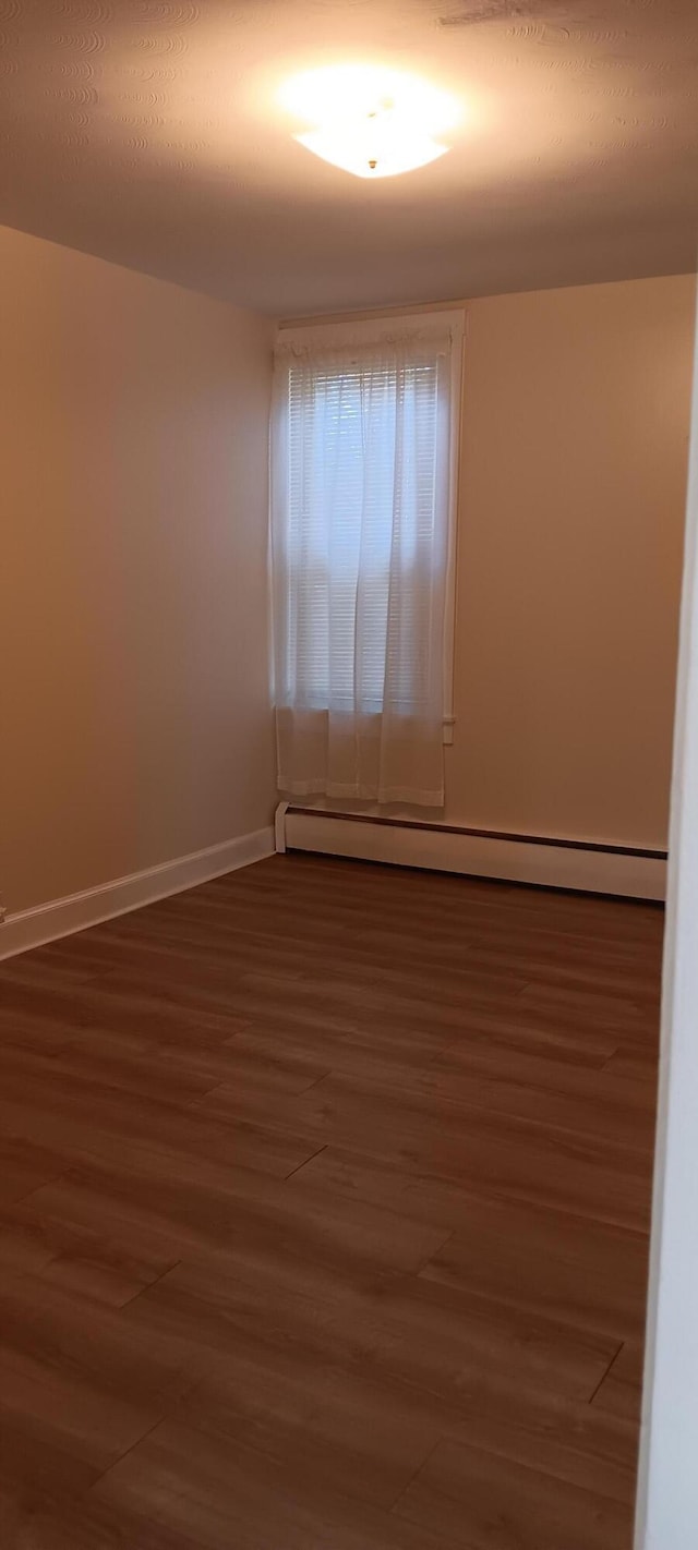 spare room featuring baseboard heating, baseboards, and wood finished floors