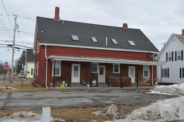 view of front facade featuring entry steps, covered porch, a shingled roof, and a chimney