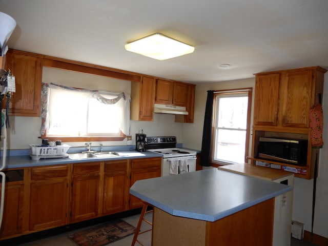 kitchen with stainless steel microwave, under cabinet range hood, brown cabinets, white electric range oven, and a sink