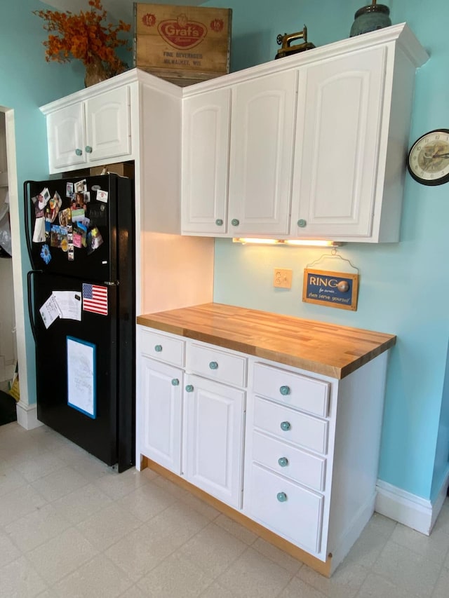 kitchen featuring wood counters, baseboards, white cabinets, freestanding refrigerator, and light floors