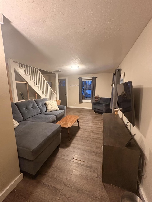 living room featuring stairway, dark wood-style floors, baseboards, and a textured ceiling