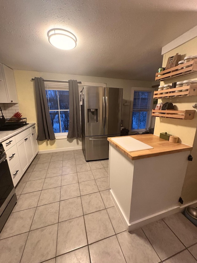 kitchen with stainless steel refrigerator with ice dispenser, light tile patterned flooring, stove, white cabinets, and a sink