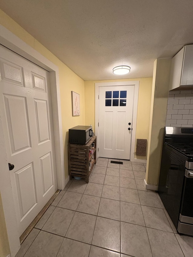 doorway featuring light tile patterned floors, a textured ceiling, and baseboards