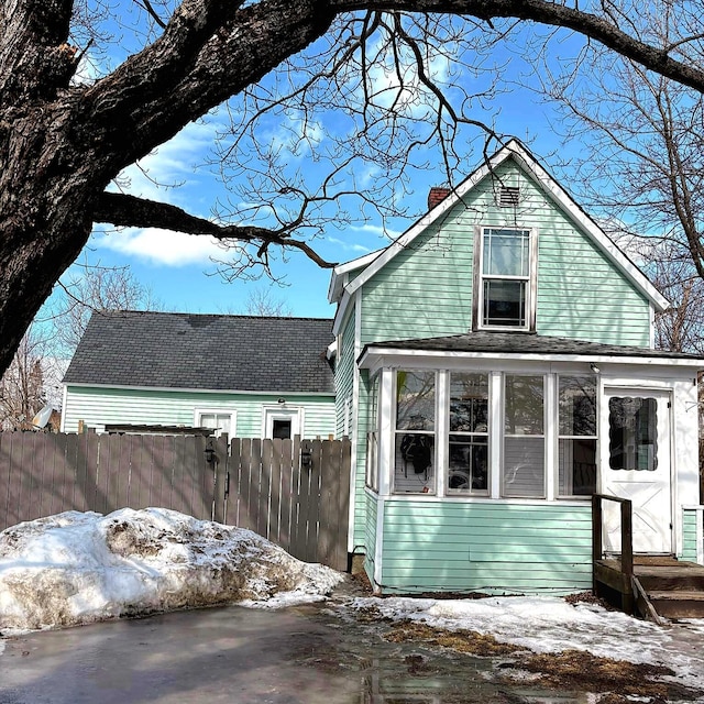 snow covered property featuring a chimney, a sunroom, and fence