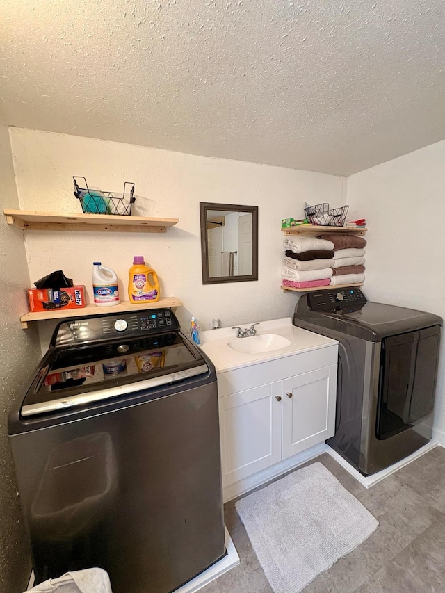 clothes washing area featuring a sink, a textured ceiling, cabinet space, and washer and clothes dryer