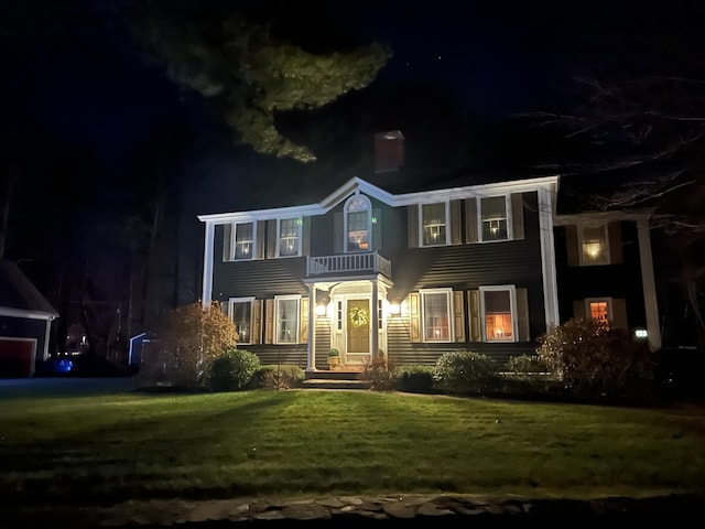 front of house at twilight with a balcony and a yard