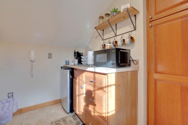 bar featuring light tile patterned floors, baseboards, refrigerator, vaulted ceiling, and black microwave