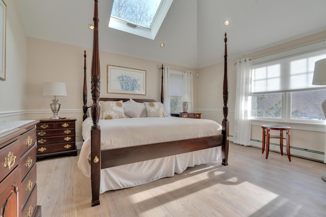 bedroom with a baseboard heating unit, light wood-style floors, a skylight, and high vaulted ceiling