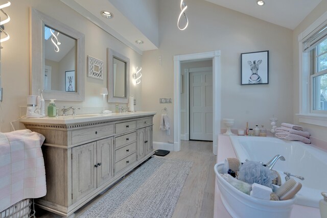 full bath featuring a garden tub, a sink, wood finished floors, double vanity, and vaulted ceiling