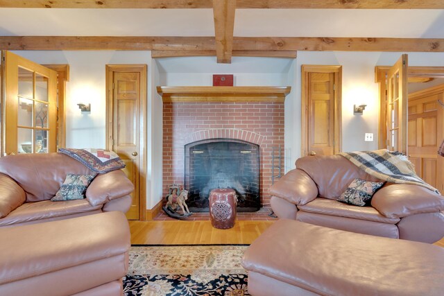 living room with beam ceiling, a brick fireplace, and wood finished floors