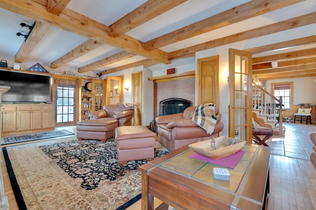 living room featuring stairs, beam ceiling, a brick fireplace, and wood-type flooring