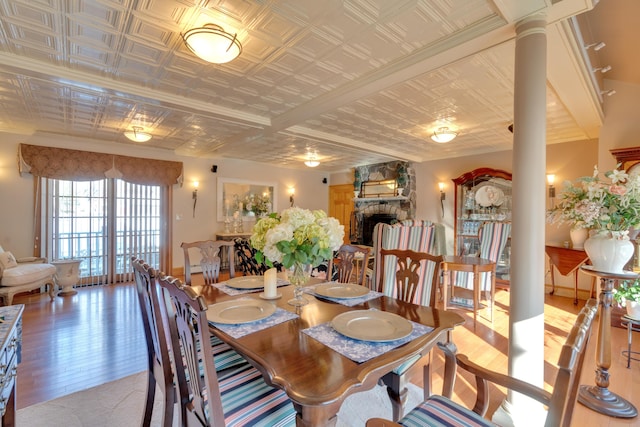 dining space with a stone fireplace, wood finished floors, ornate columns, and an ornate ceiling