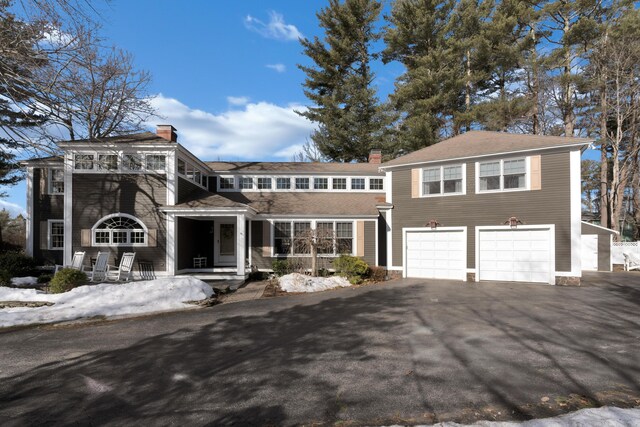 shingle-style home with aphalt driveway, a chimney, and a garage