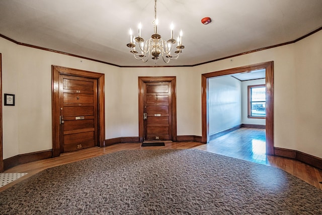 empty room with a chandelier, crown molding, baseboards, and wood finished floors