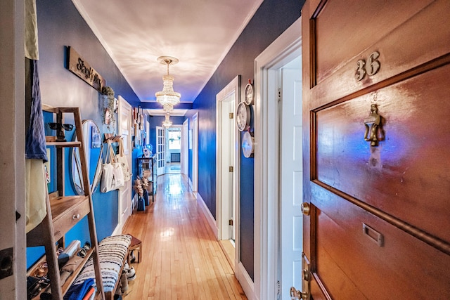 hallway with baseboards, an inviting chandelier, and light wood finished floors