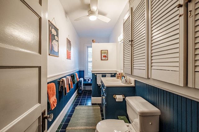 bathroom with a wainscoted wall, toilet, tile patterned floors, vanity, and a ceiling fan