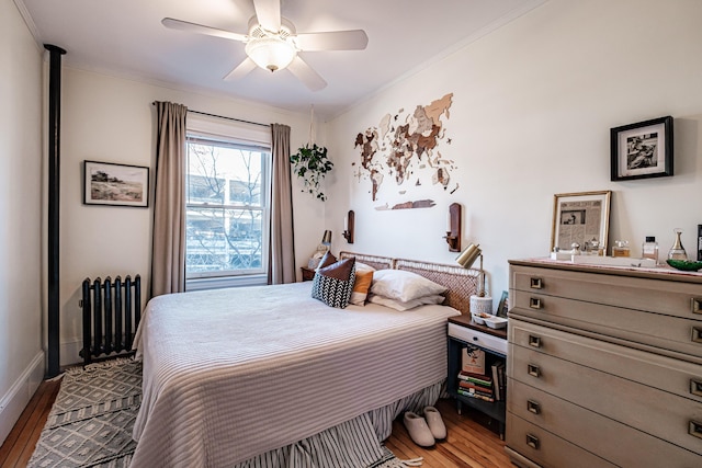 bedroom with ornamental molding, wood finished floors, radiator heating unit, baseboards, and ceiling fan