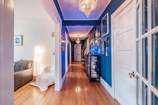 hall with baseboards, a chandelier, and hardwood / wood-style flooring