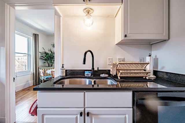 kitchen with dishwashing machine, white cabinets, wood finished floors, and a sink