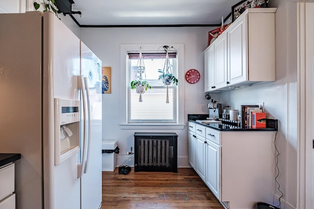 kitchen with dark countertops, crown molding, white refrigerator with ice dispenser, dark wood-style floors, and white cabinetry