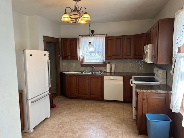 kitchen featuring dark countertops, backsplash, brown cabinets, white appliances, and a sink