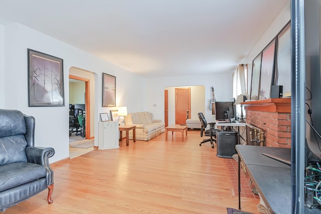 office area featuring a fireplace, arched walkways, and light wood-type flooring