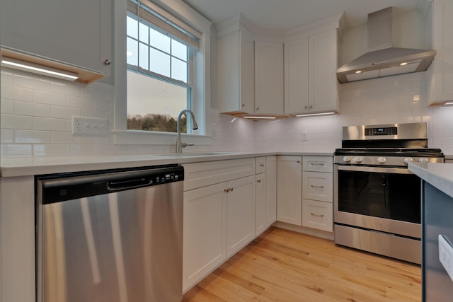 kitchen with light countertops, appliances with stainless steel finishes, light wood-style floors, wall chimney exhaust hood, and a sink