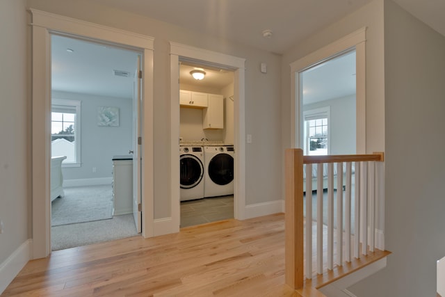 corridor with visible vents, an upstairs landing, light wood-style floors, and washing machine and dryer