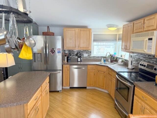 kitchen featuring light wood-style flooring, light brown cabinetry, decorative backsplash, a sink, and appliances with stainless steel finishes