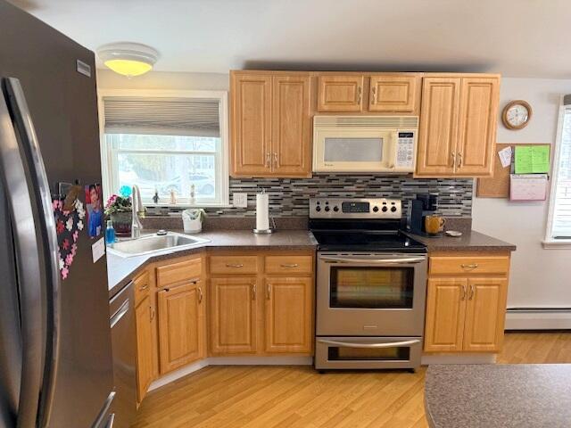 kitchen with a sink, appliances with stainless steel finishes, light wood finished floors, decorative backsplash, and baseboard heating