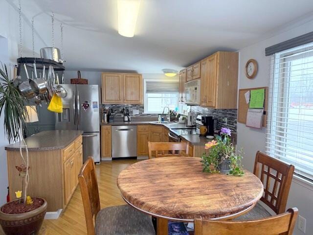 kitchen featuring light brown cabinets, a sink, decorative backsplash, stainless steel appliances, and light wood-style floors